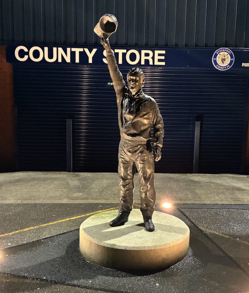 A photograph of the Danny Bergara statue lit up at night time outside Edgeley Park.
