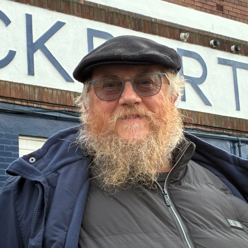 A photo of John Bilsbury from Stockport County Supporters Cooperative stood outside the Stockport County sign at Edgeley Park, Stockport.